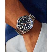 Load image into Gallery viewer, Wrist wearing a silver and blue watch with a brand logo on a neutral background