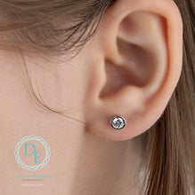 Load image into Gallery viewer, Close-up of an ear wearing a diamond stud earring with a visible brand logo.