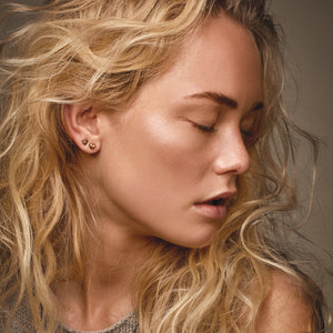 Close-up of a woman with blonde hair and earrings against a neutral background