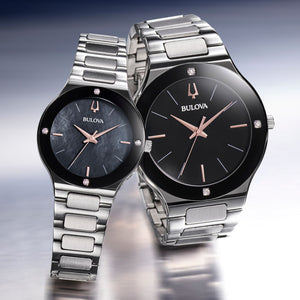 Two Bulova watches with black faces and silver metal bands on a gradient background