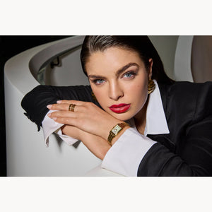 Woman in formal attire with jewelry leaning against a white wall