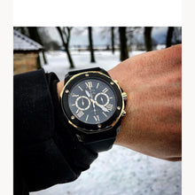 Load image into Gallery viewer, Black watch with gold accents on a wrist against a snowy background
