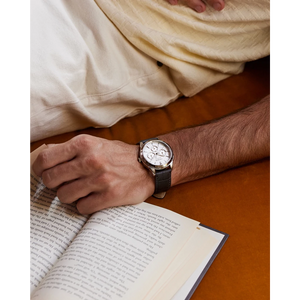 Person wearing a watch on a wooden surface with an open book