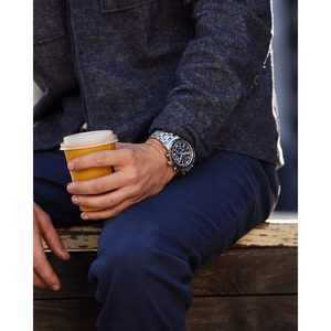 Person holding a coffee cup with a watch on a wooden bench