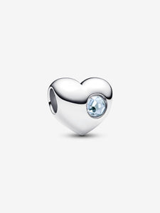 Heart-shaped silver charm with a pale blue gemstone on a white background