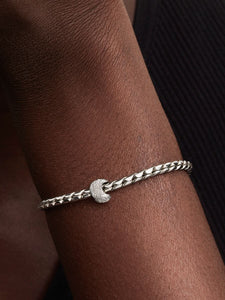 Silver bracelet with a moon charm on a wrist against a dark background