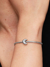 Load image into Gallery viewer, Silver bracelet with a moon charm on a wrist against a black background
