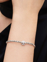 Load image into Gallery viewer, Silver bracelet with a skull charm on a wrist against a black background
