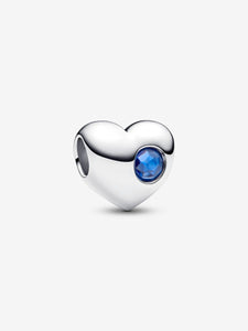 Heart-shaped silver charm with a blue gemstone on a white background