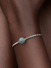 Load image into Gallery viewer, Silver bracelet with a blue charm on a wrist against a brown background
