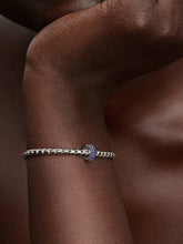 Load image into Gallery viewer, Gold bracelet with a blue gemstone on a wrist against a brown background

