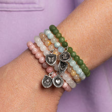 Load image into Gallery viewer, Stack of beaded bracelets with charms on a wrist against a purple background
