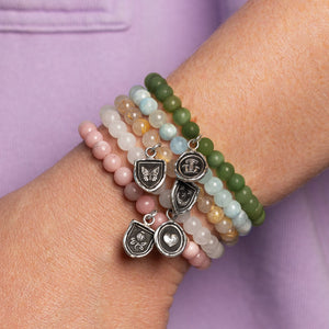 Stack of beaded bracelets with charms on a wrist against a purple background